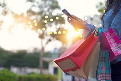 A woman is holding shopping bags and using a cell phone.