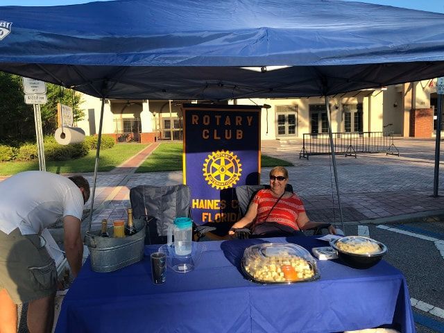 A woman sits at a table under a canopy that says rotary club