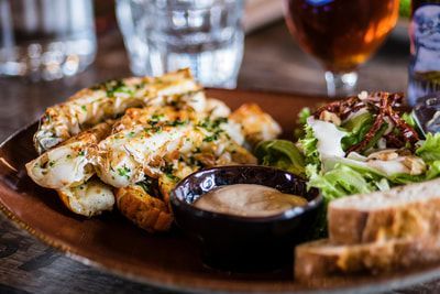 A close up of a plate of food on a table with a glass of beer in the background.