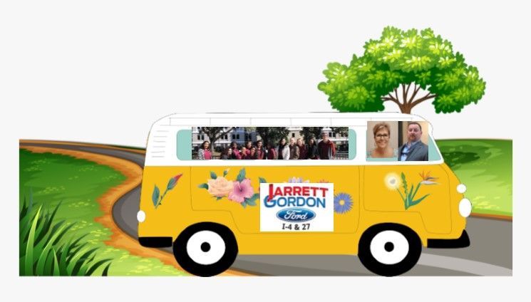 A yellow van is driving down a road with a tree in the background.