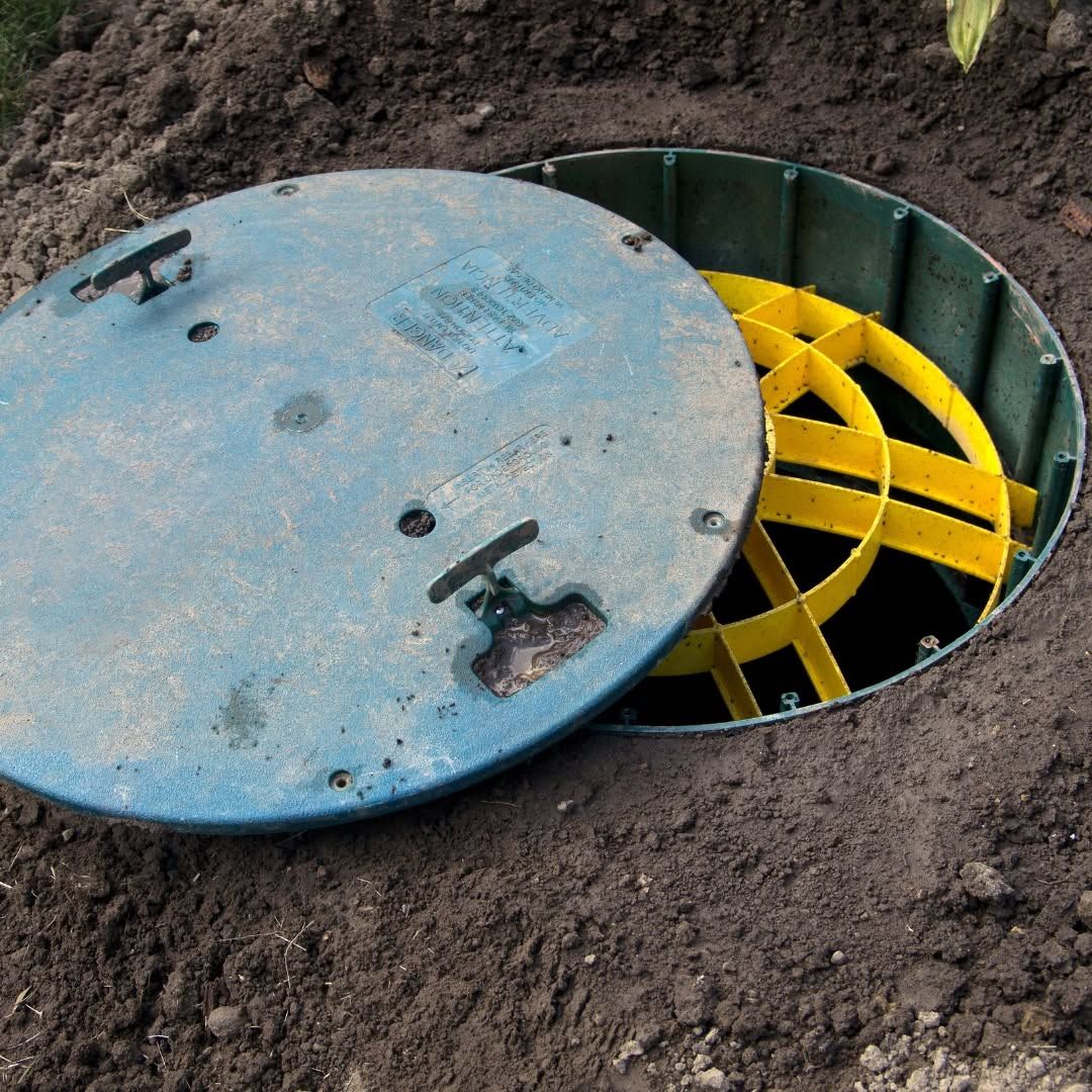 Partially open manhole in dirt, showing yellow underground chamber beneath a blue cover