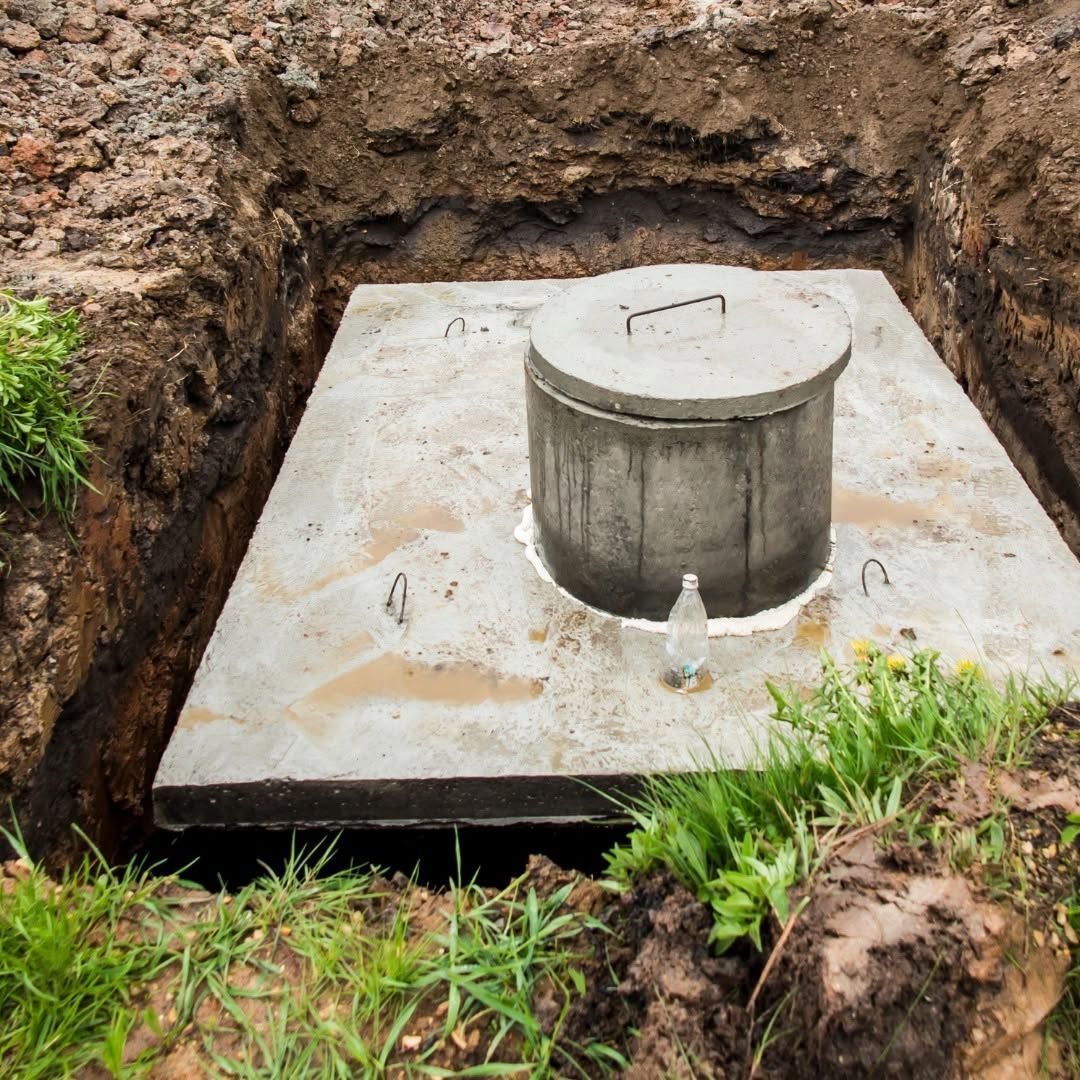 Concrete utility cover in an earthen pit, surrounded by grass and dirt.