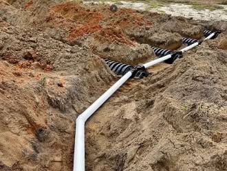 White pipeline with black-striped protective covering crossing a sandy trench at a construction site