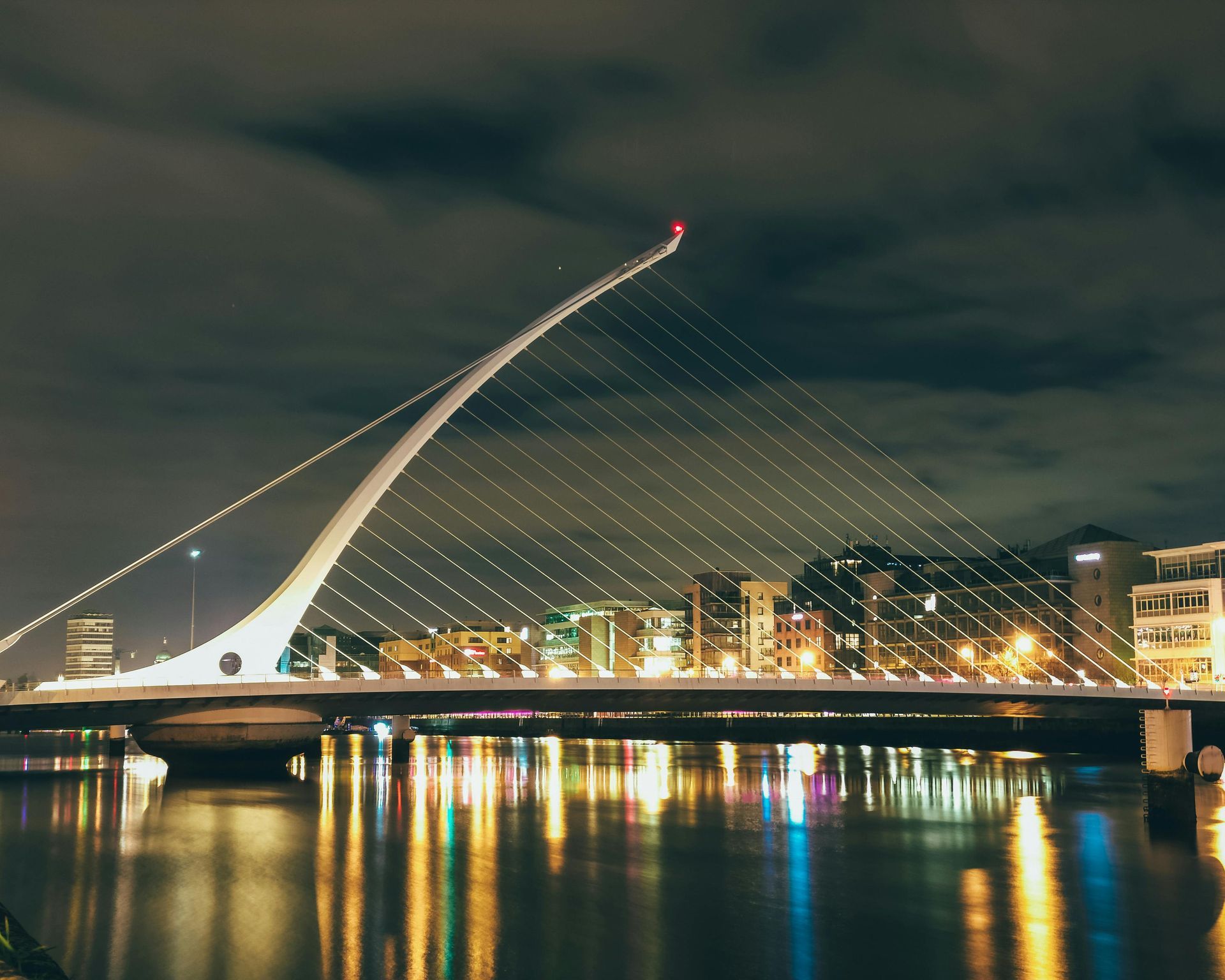 Night city bridge with a white illuminated cable tower reflected in calm water