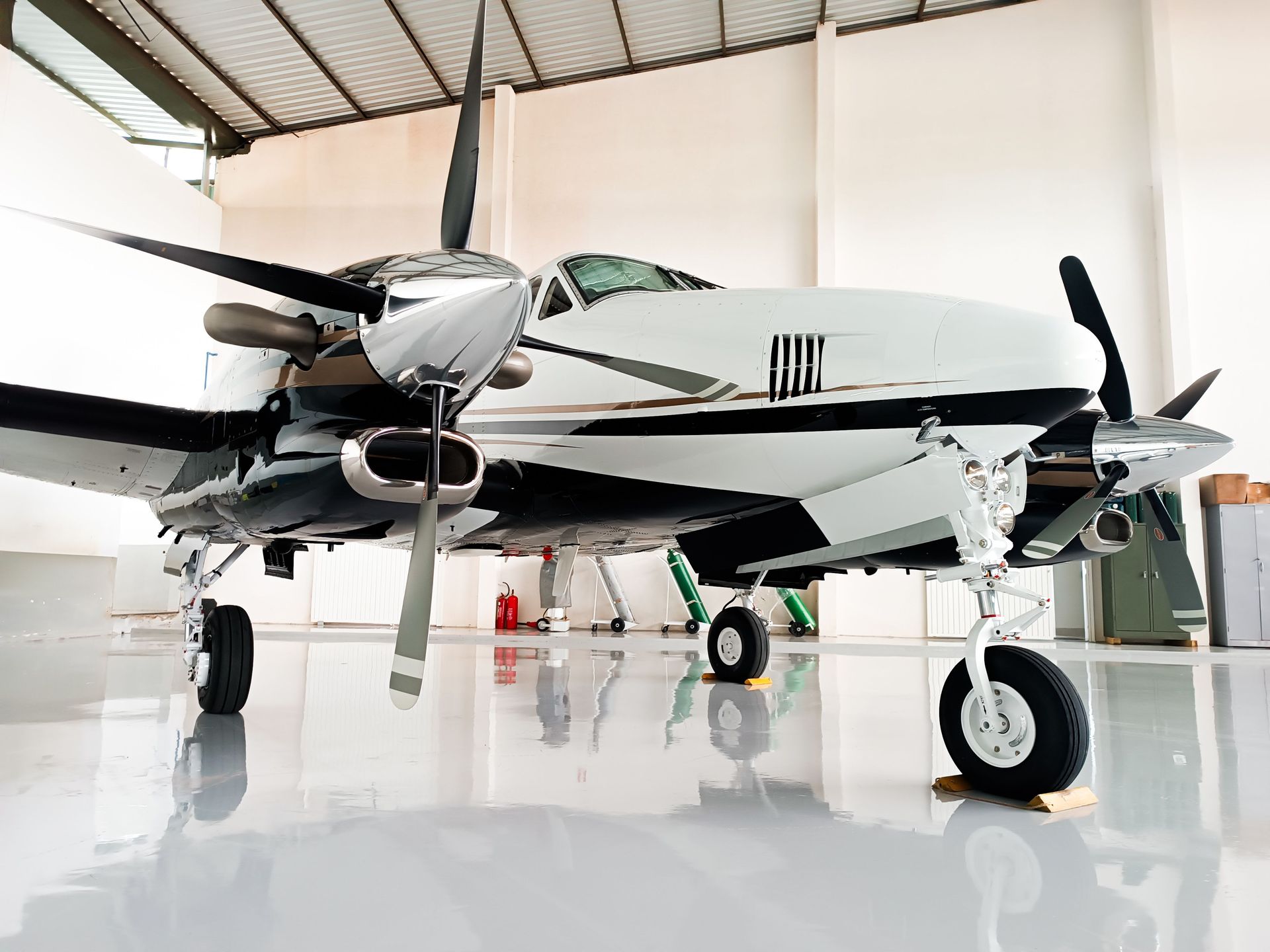Twin-engine propeller airplane in a bright hangar, viewed from the front-left side