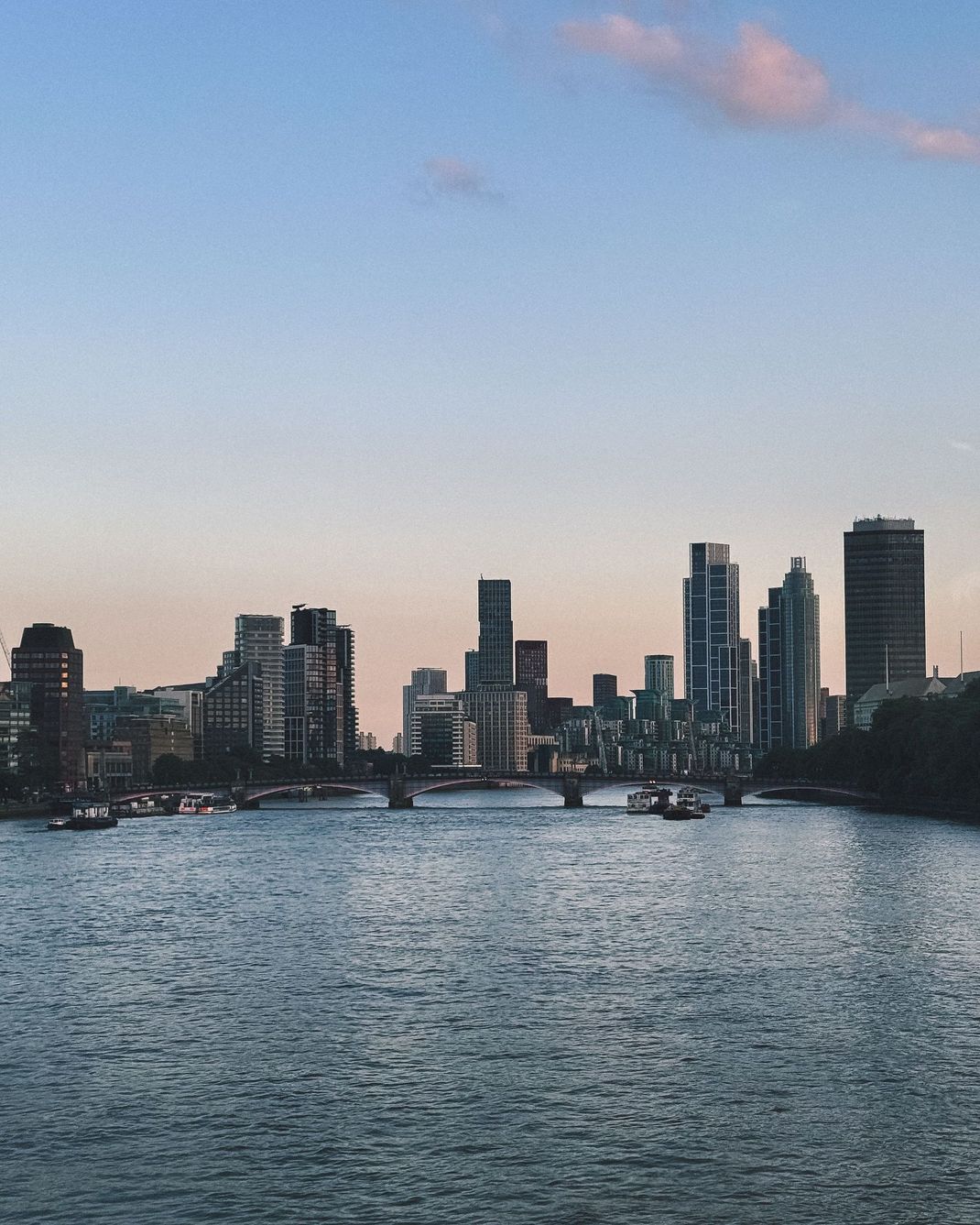 City skyline at dusk reflected on a rippling river, with buildings silhouetted against a pastel sky.