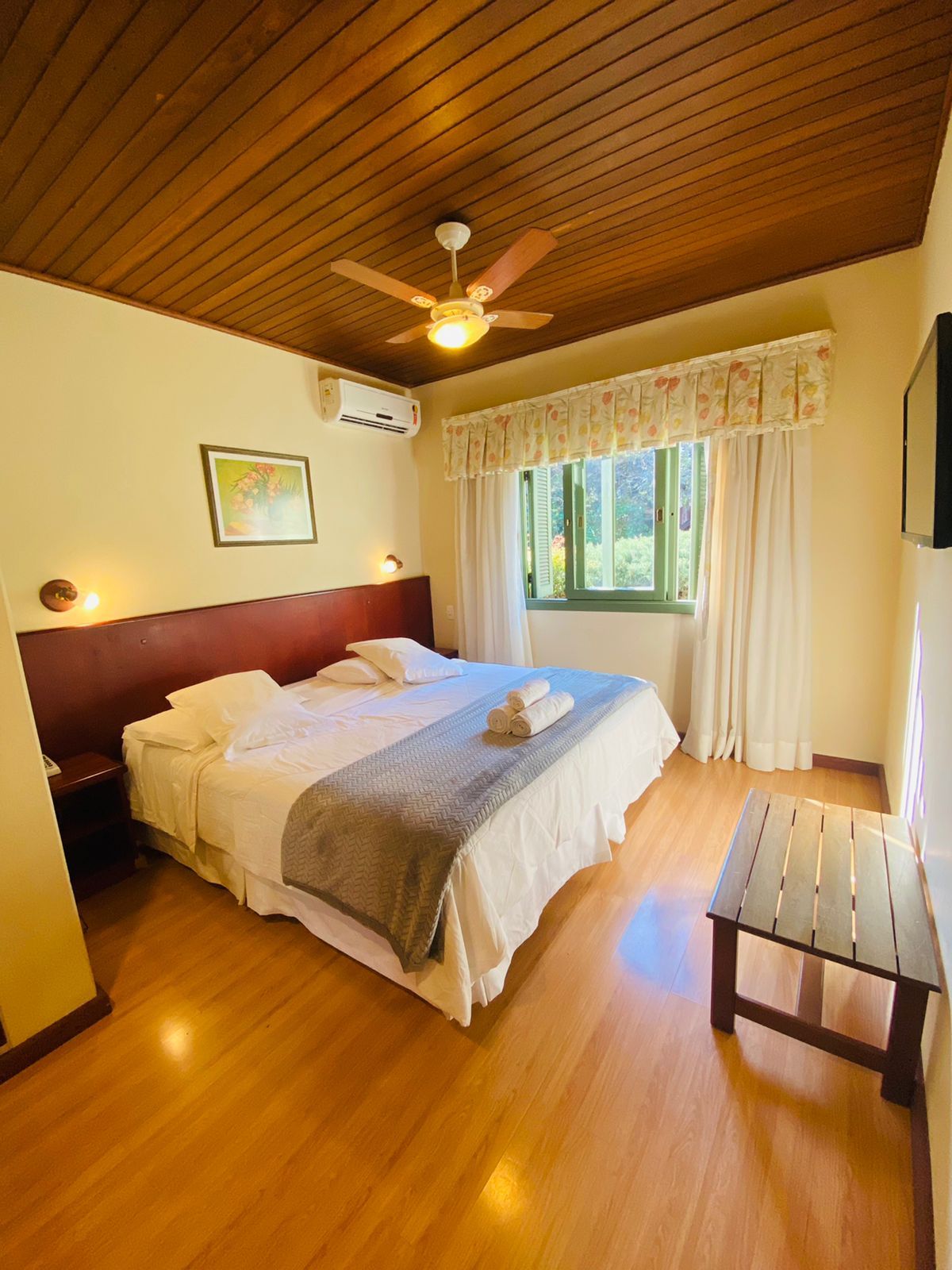 Um quarto de hotel com cama king size, ventilador de teto, mesa e janela.