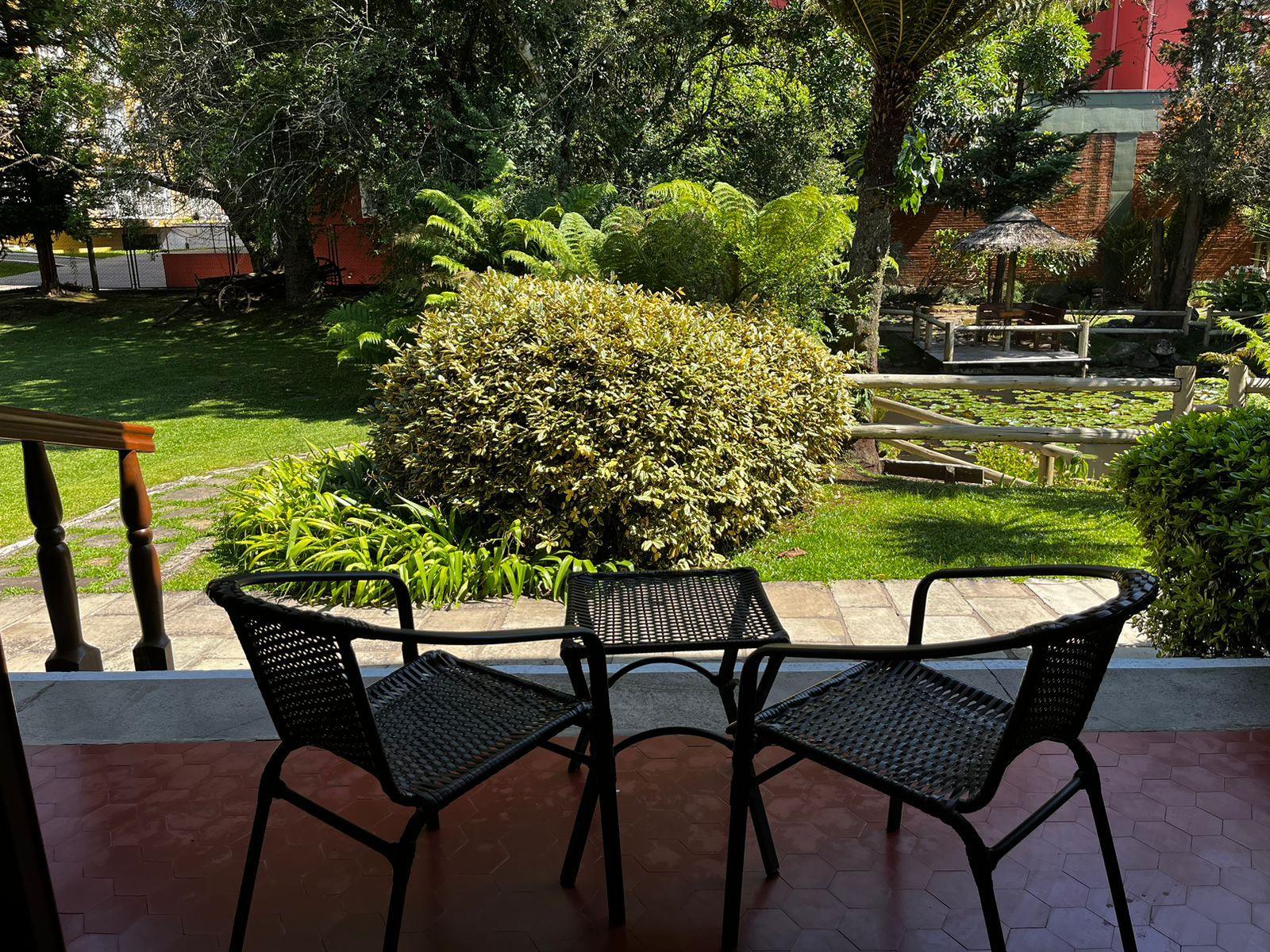 Duas cadeiras e uma mesa numa varanda com vista para um jardim.