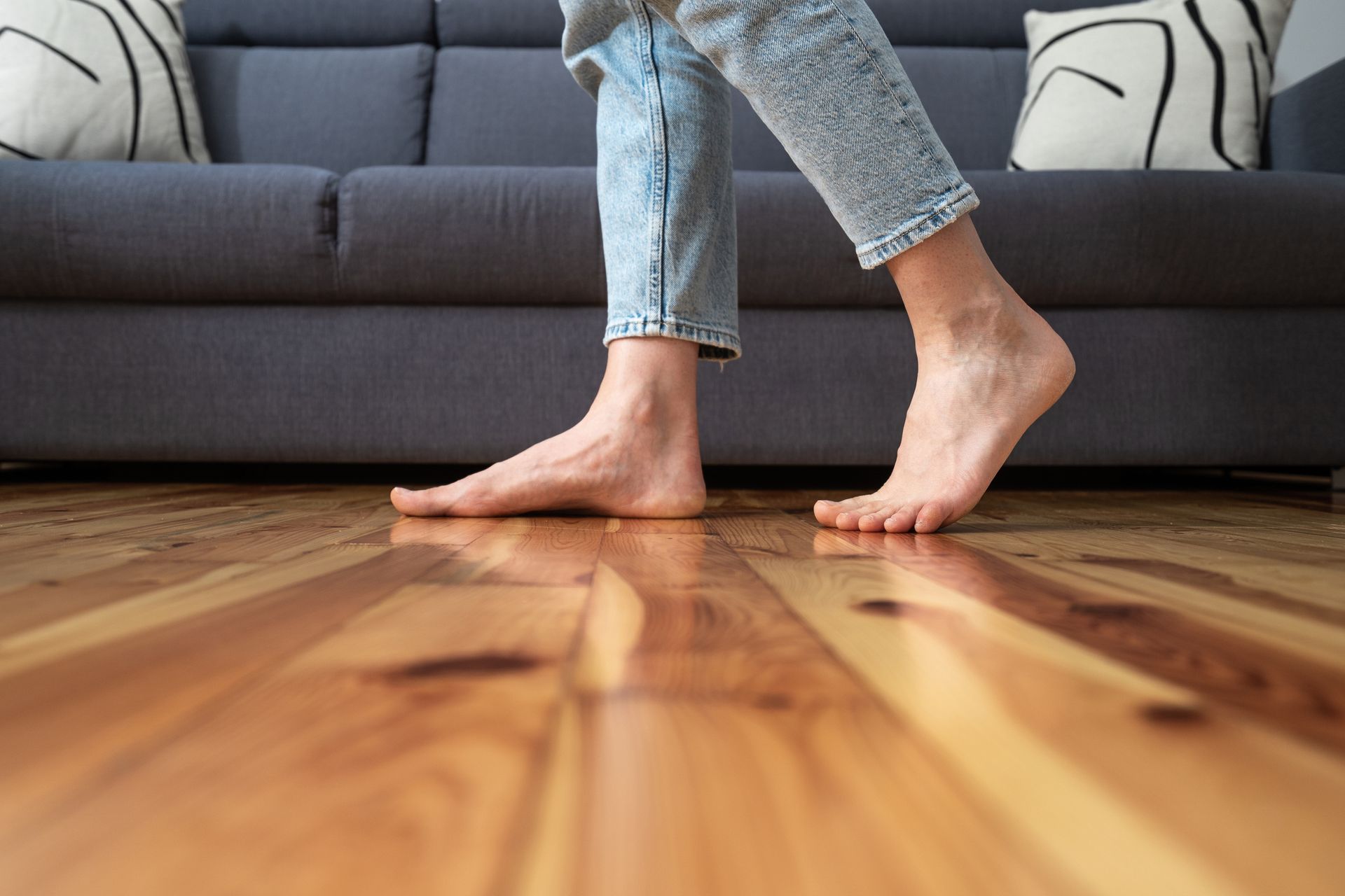A Person Is Walking Barefoot on A Wooden Floor In A Living Room — Greensboro, NC — Blackdog Handyman Service Inc.
