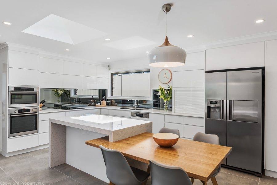 Bright modern kitchen with white cabinets, stainless steel fridge, and wooden dining table