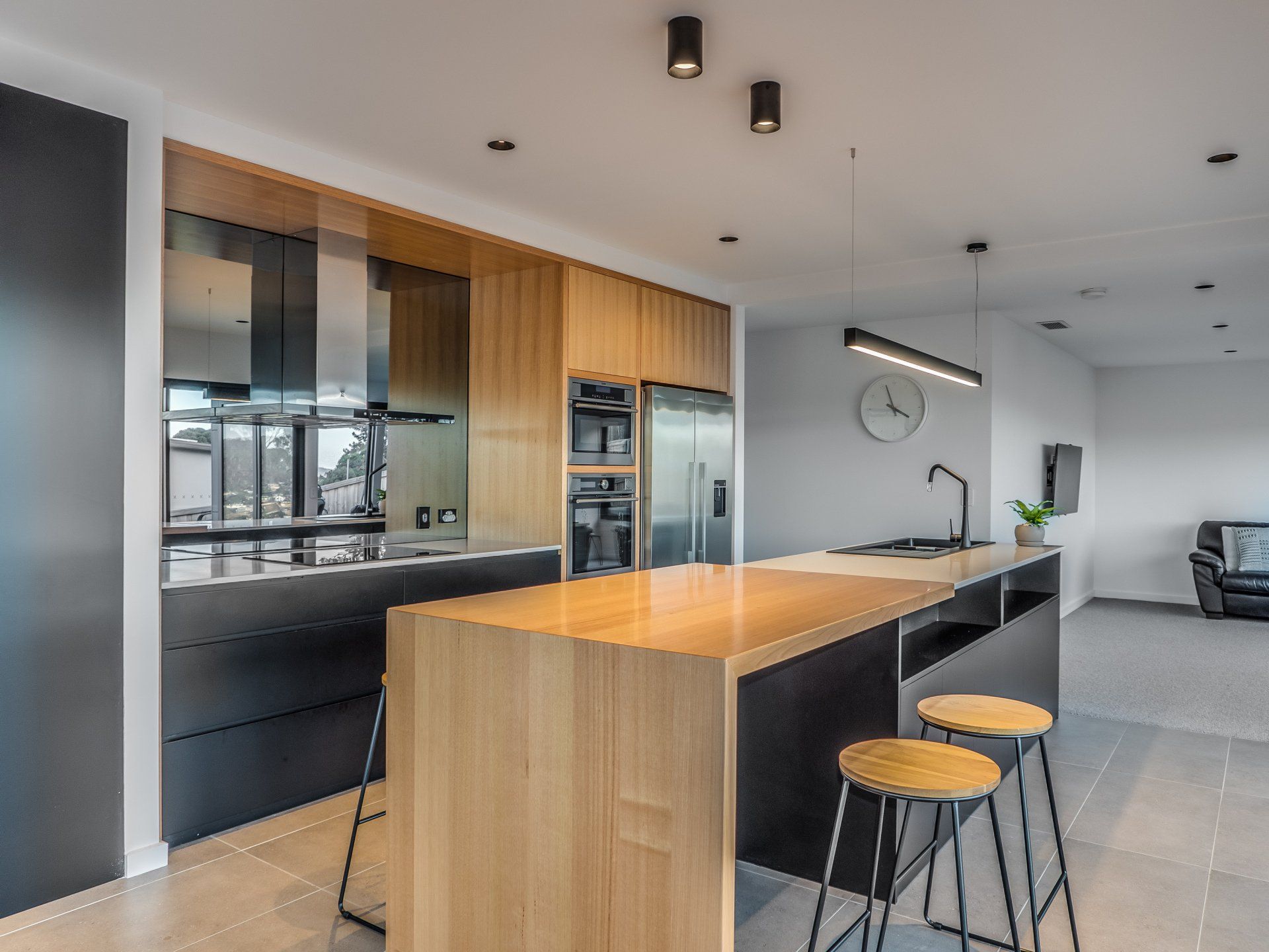 Modern open-plan kitchen with wood island, black stools, and built-in appliances