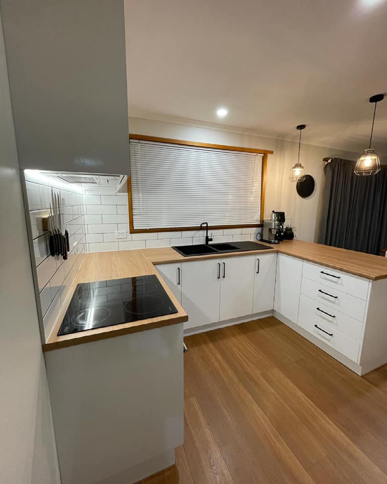 Modern white kitchen with wood countertops, black sink, and warm pendant lights.