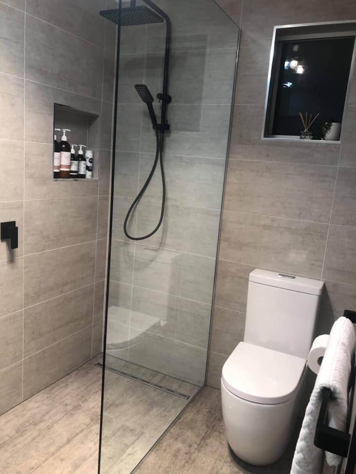 Modern bathroom with glass shower, white toilet, gray tiles, and wall-mounted toiletries.