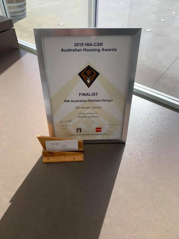 Framed finalist award plaque on a table by a window, with a small nameplate in front.