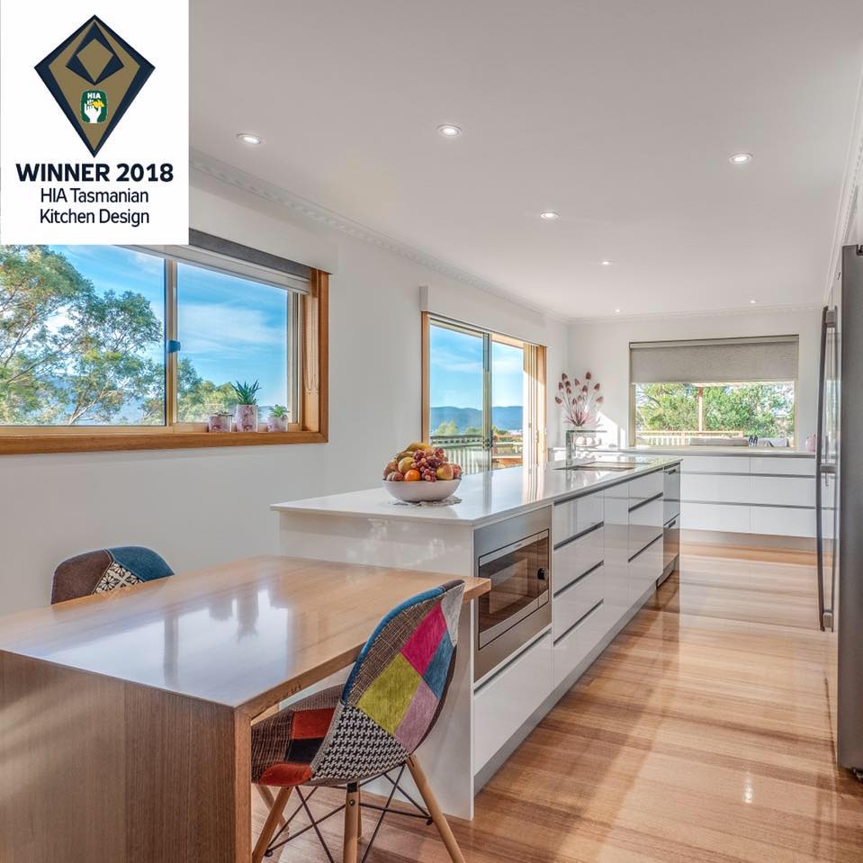 Bright modern kitchen with white island, wooden floors, large windows, and colorful chairs