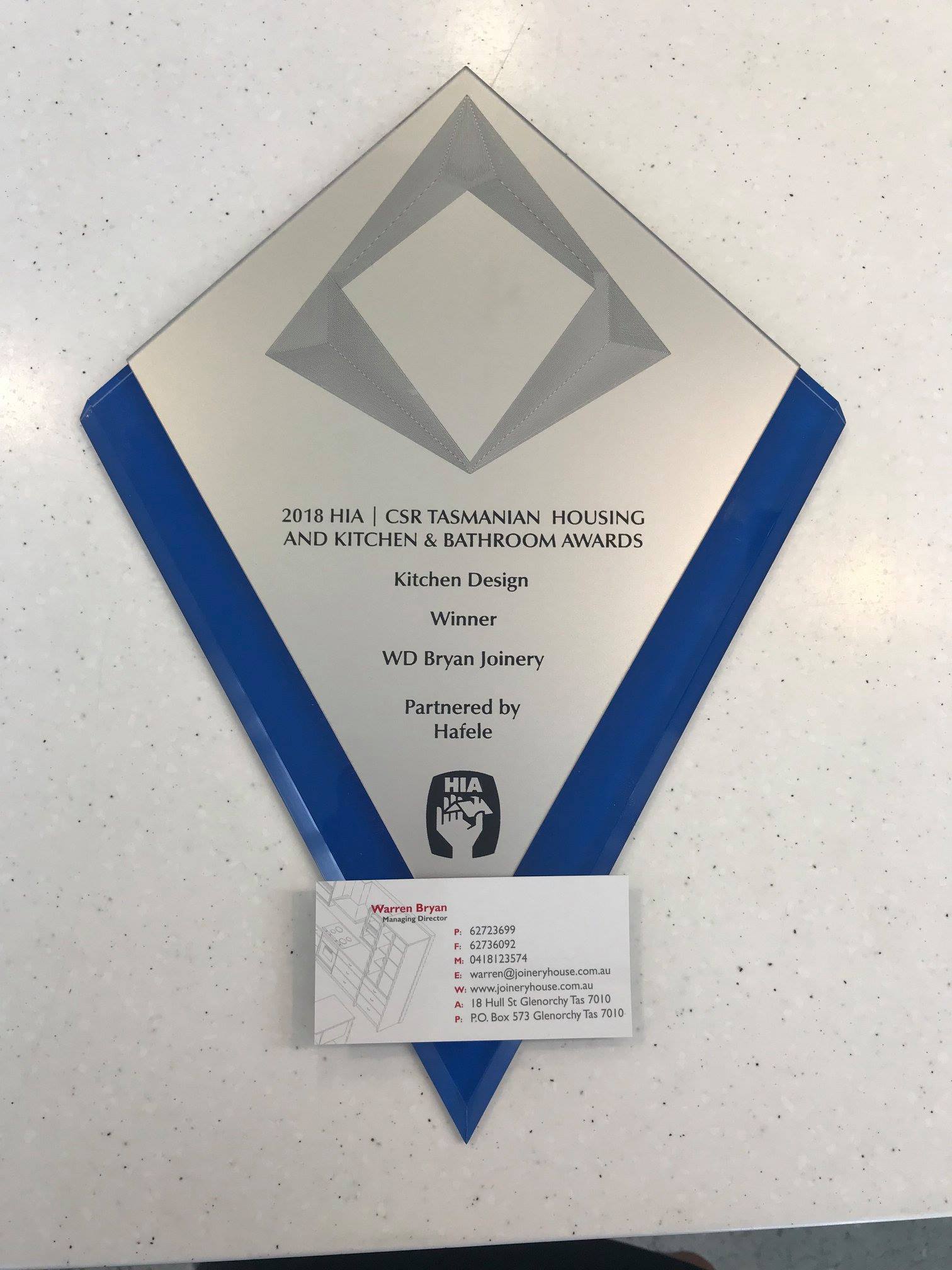Blue-and-silver diamond-shaped wall plaque with text and a small white notice below