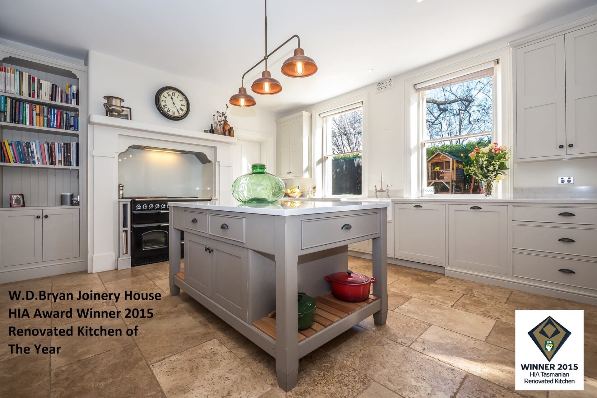 Bright white kitchen with gray island, pendant lights, built-in oven, and window plants
