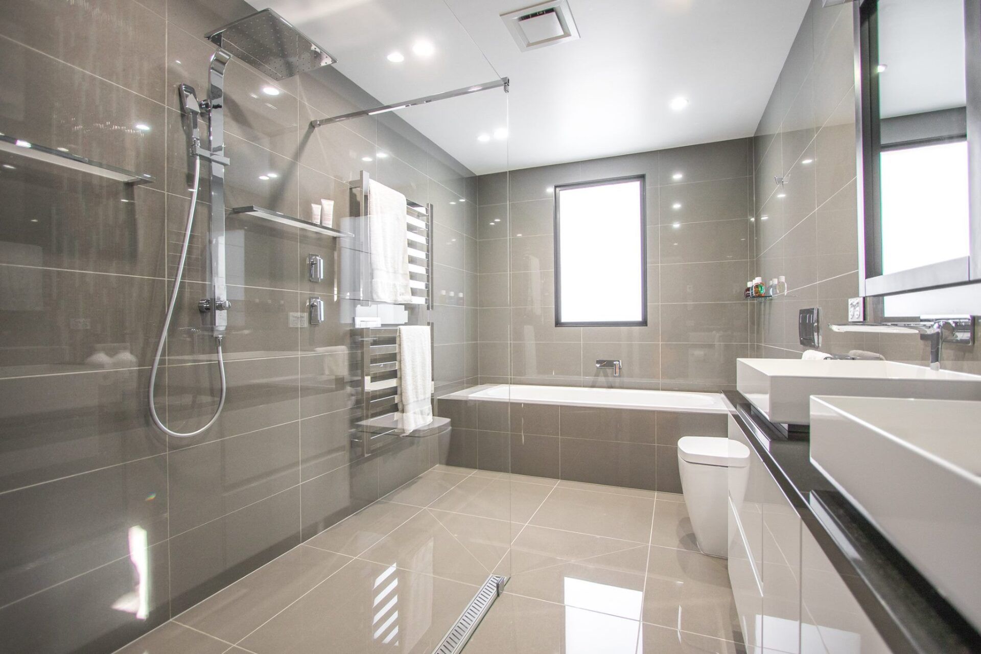 Modern gray-tiled bathroom with glass shower, bathtub, and large window