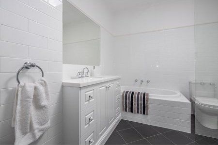 Bright white bathroom with vanity, mirror, towel ring, and a built-in tub with dark striped towels.