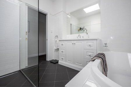 Bright white modern bathroom with black tile floor, vanity, sink, mirror, and bathtub with towels.