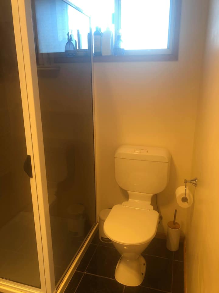 Small bathroom with a toilet, glass shower door, and window above the tank.