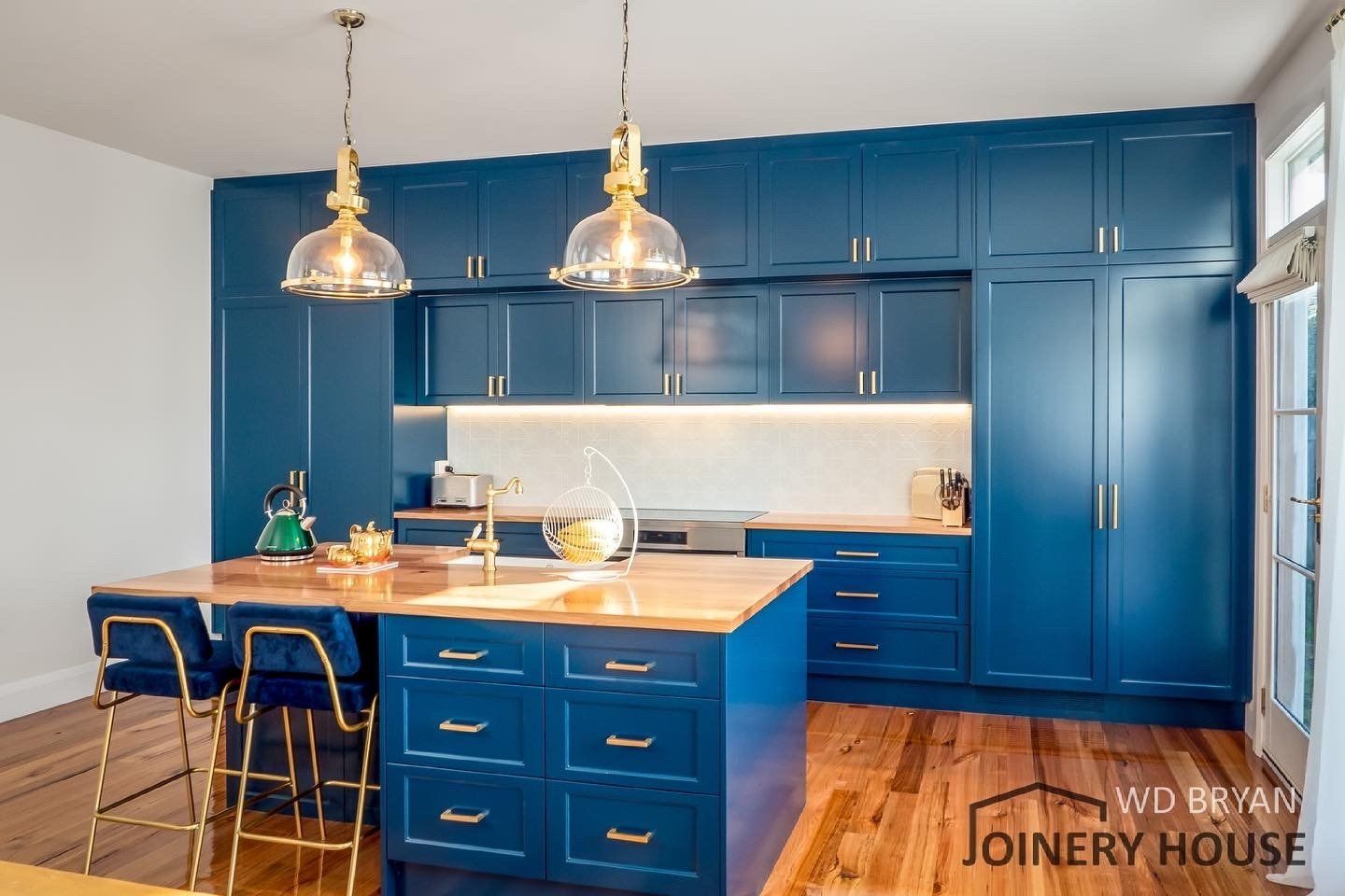 Blue kitchen with island, brass pendant lights, and wood floor in a bright modern interior