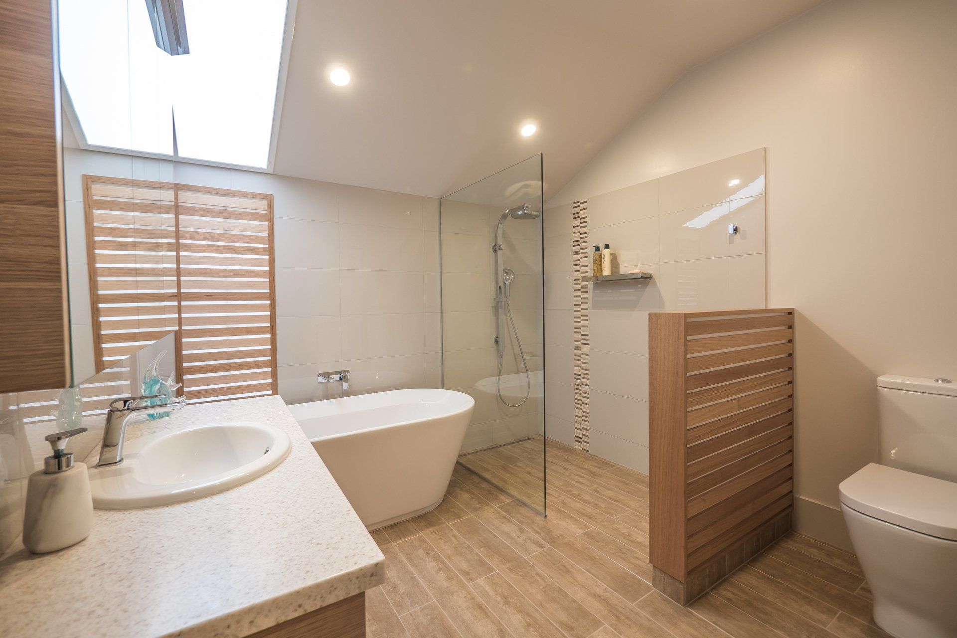 Modern bathroom with a soaking tub, glass shower, wood vanity, and toilet under skylights