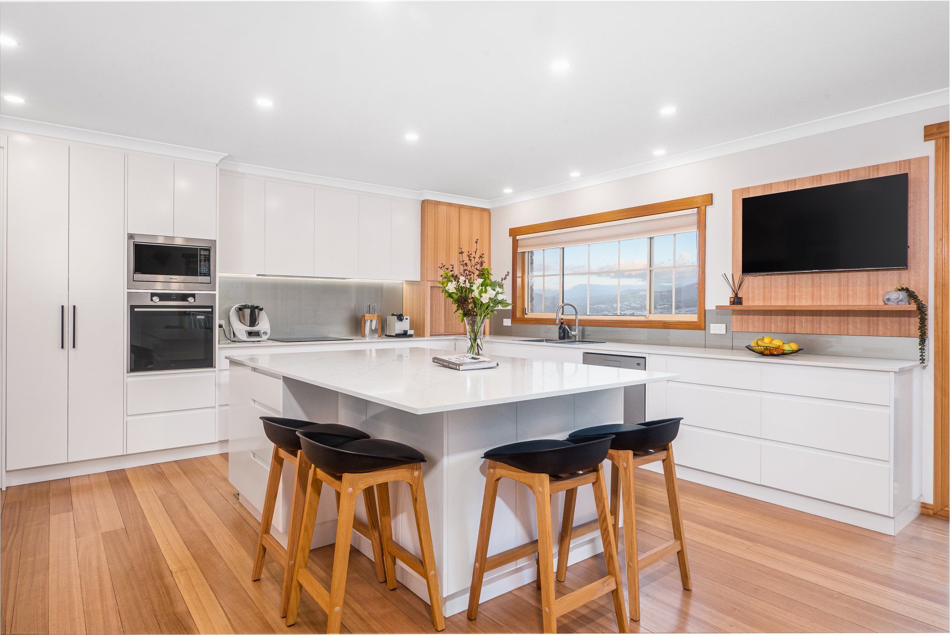 Bright modern kitchen with white cabinets, wood floors, island, and large window.