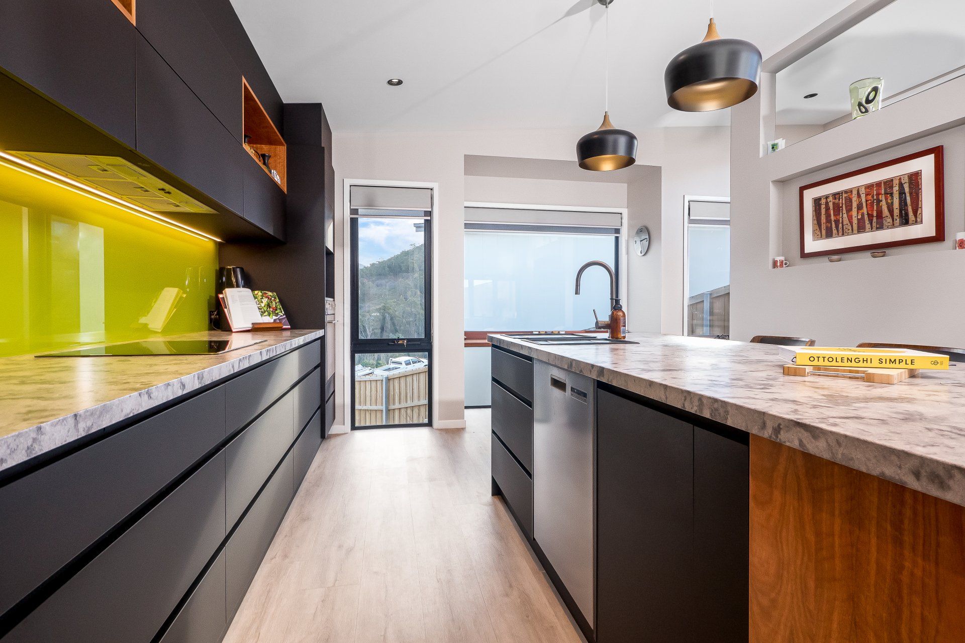 Modern kitchen with dark cabinets, wood island, granite counters, and pendant lights leading to a bright doorway