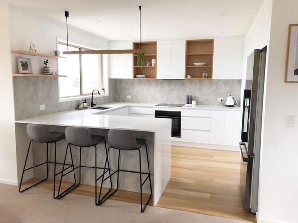 Modern white kitchen with wood accents, marble island, and three gray bar stools
