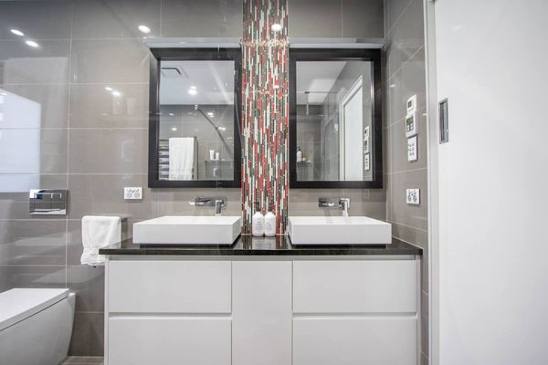 Modern bathroom vanity with double sinks, black countertop, mirrors, and gray tiled walls