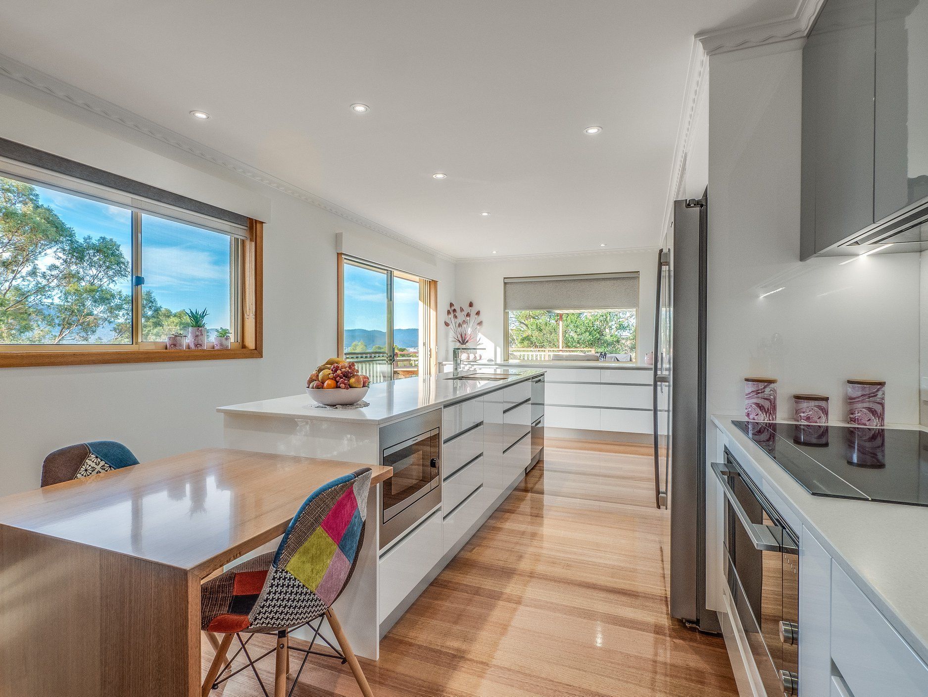 Bright modern kitchen with white cabinets, wood floors, skylights, and a colorful chair by the window