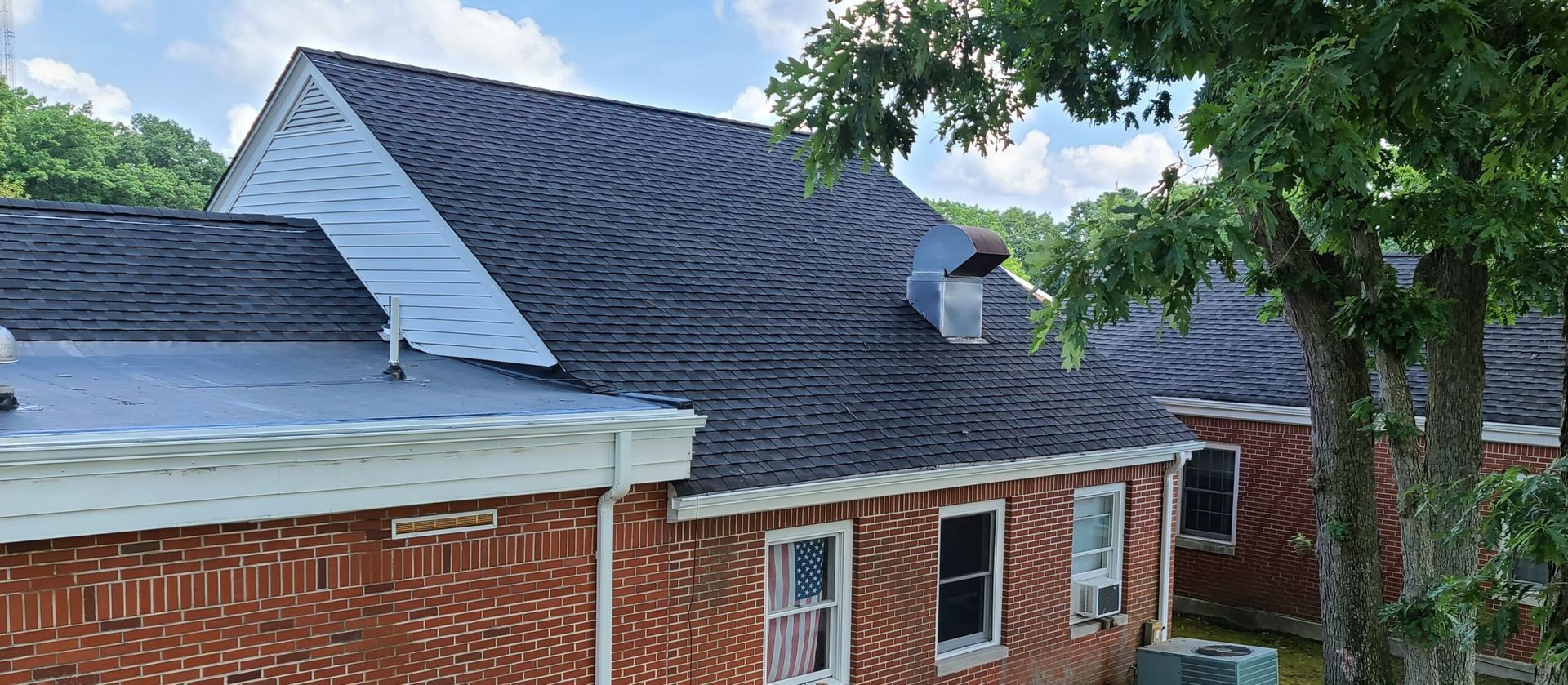 A brick house with a new roof and a tree in front of it.