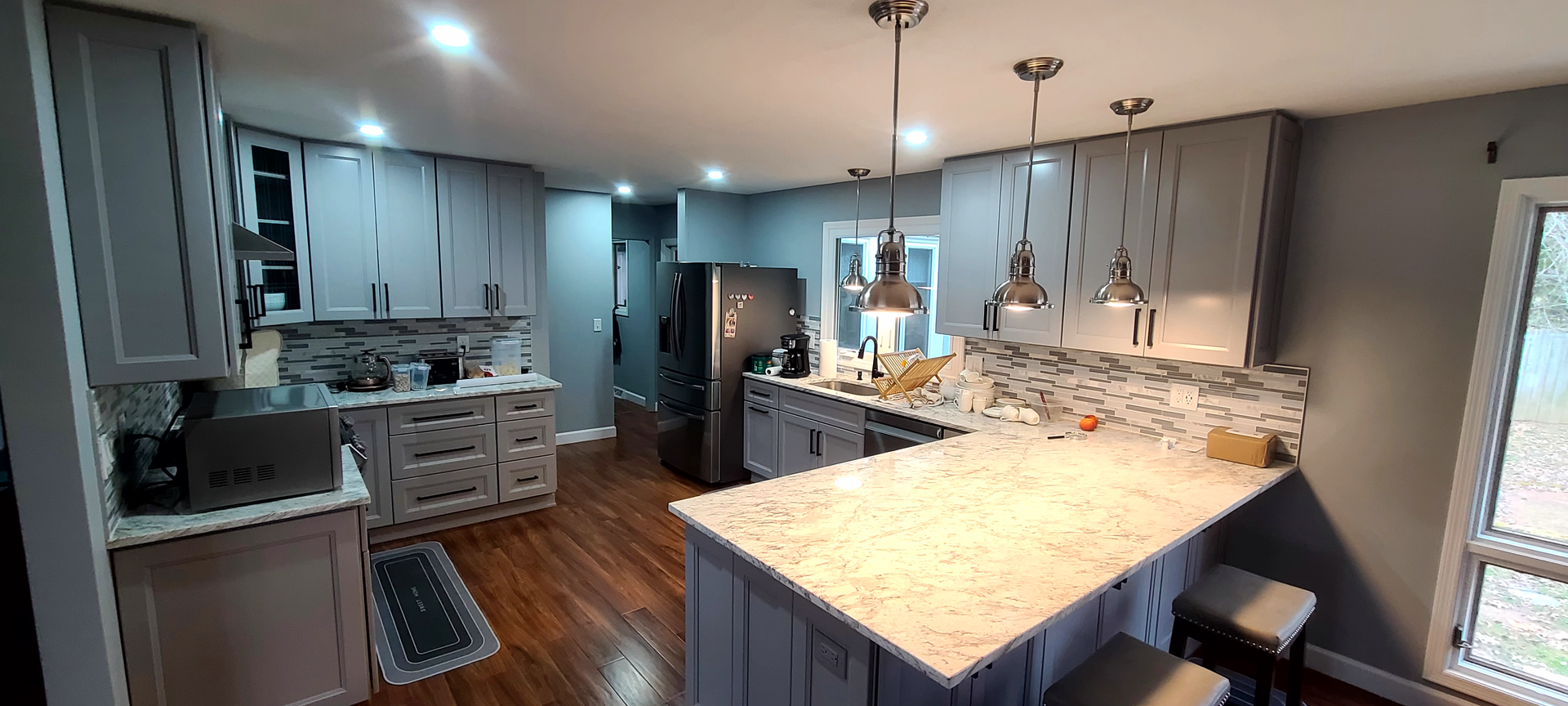 A kitchen with gray cabinets , granite counter tops , stainless steel appliances and a large island.