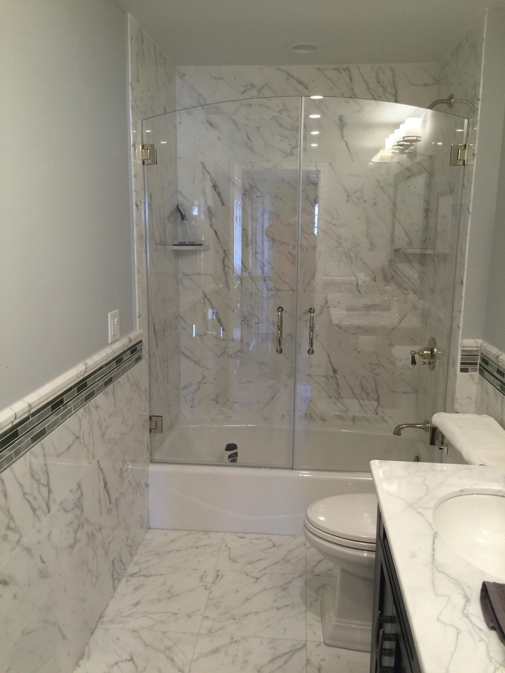 A bathroom with marble tiles , a toilet , sink and shower.