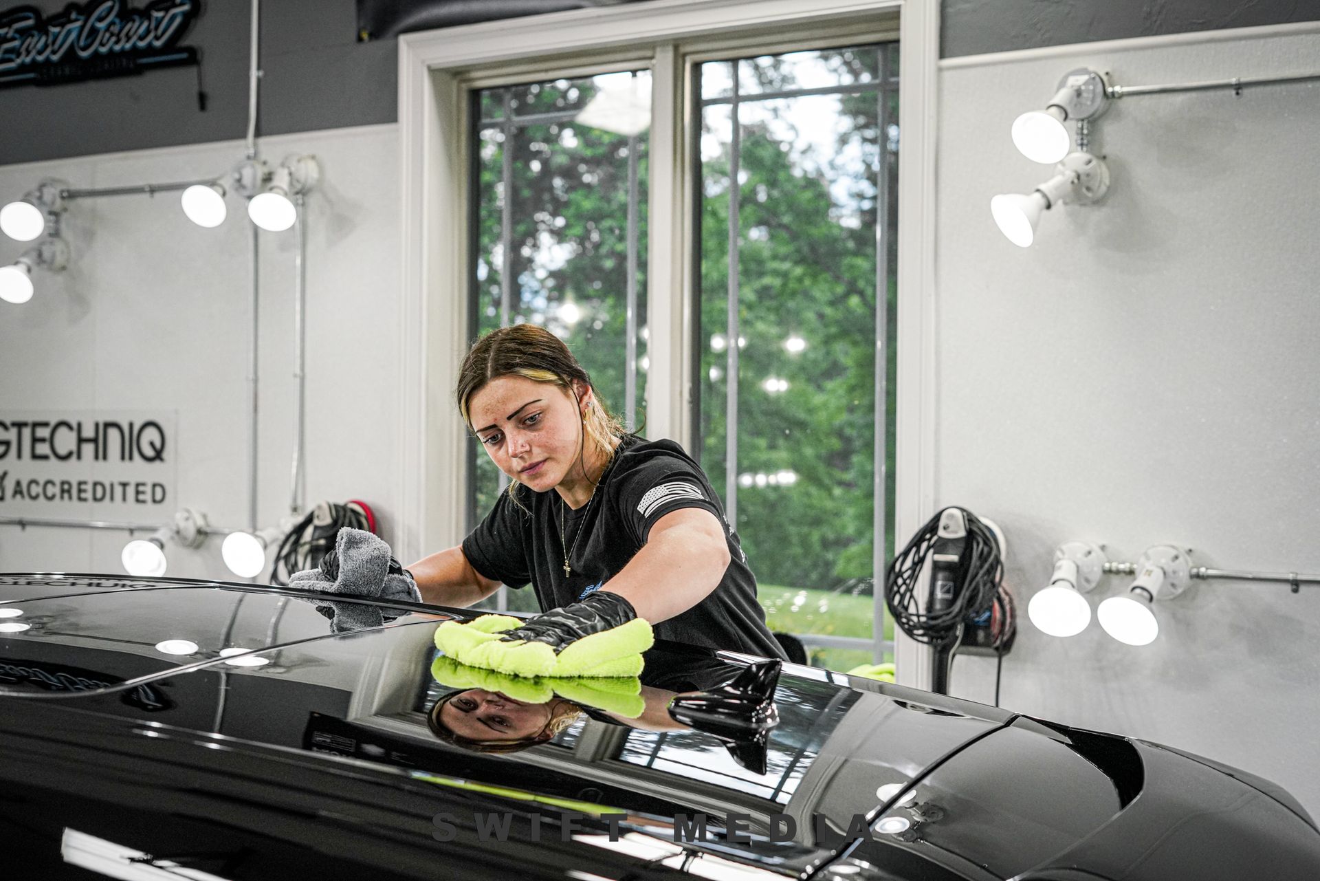 A woman is polishing a car in a garage.