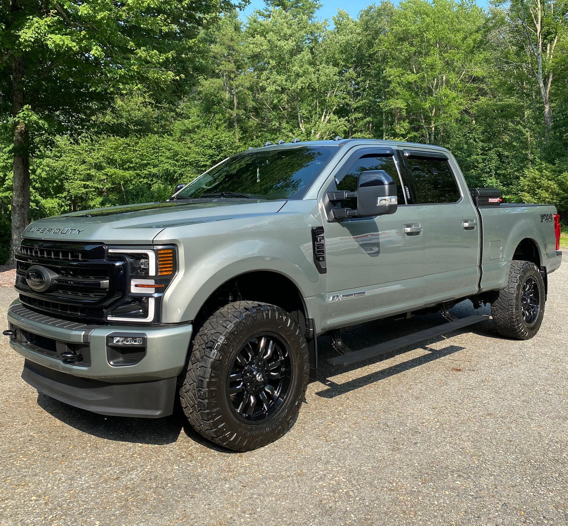 A gray ford truck is parked in a gravel lot in front of trees.