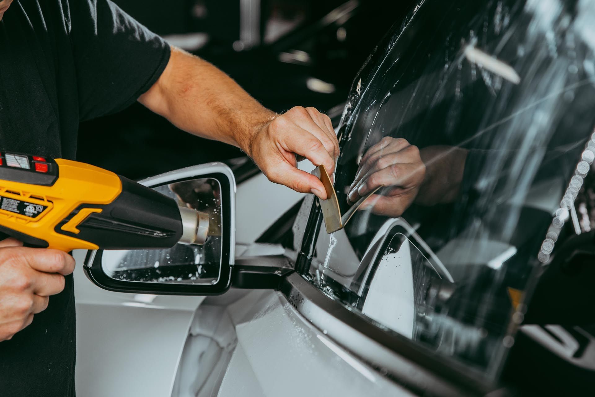 A person is applying tinted window film to a car window.
