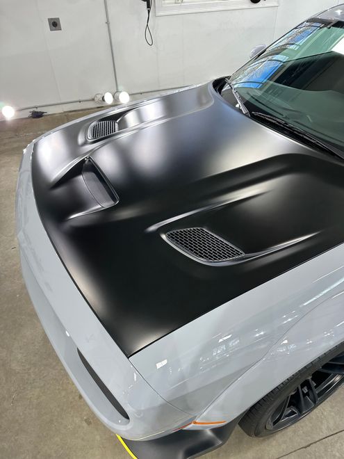 A white dodge challenger with a black hood is parked in a garage.