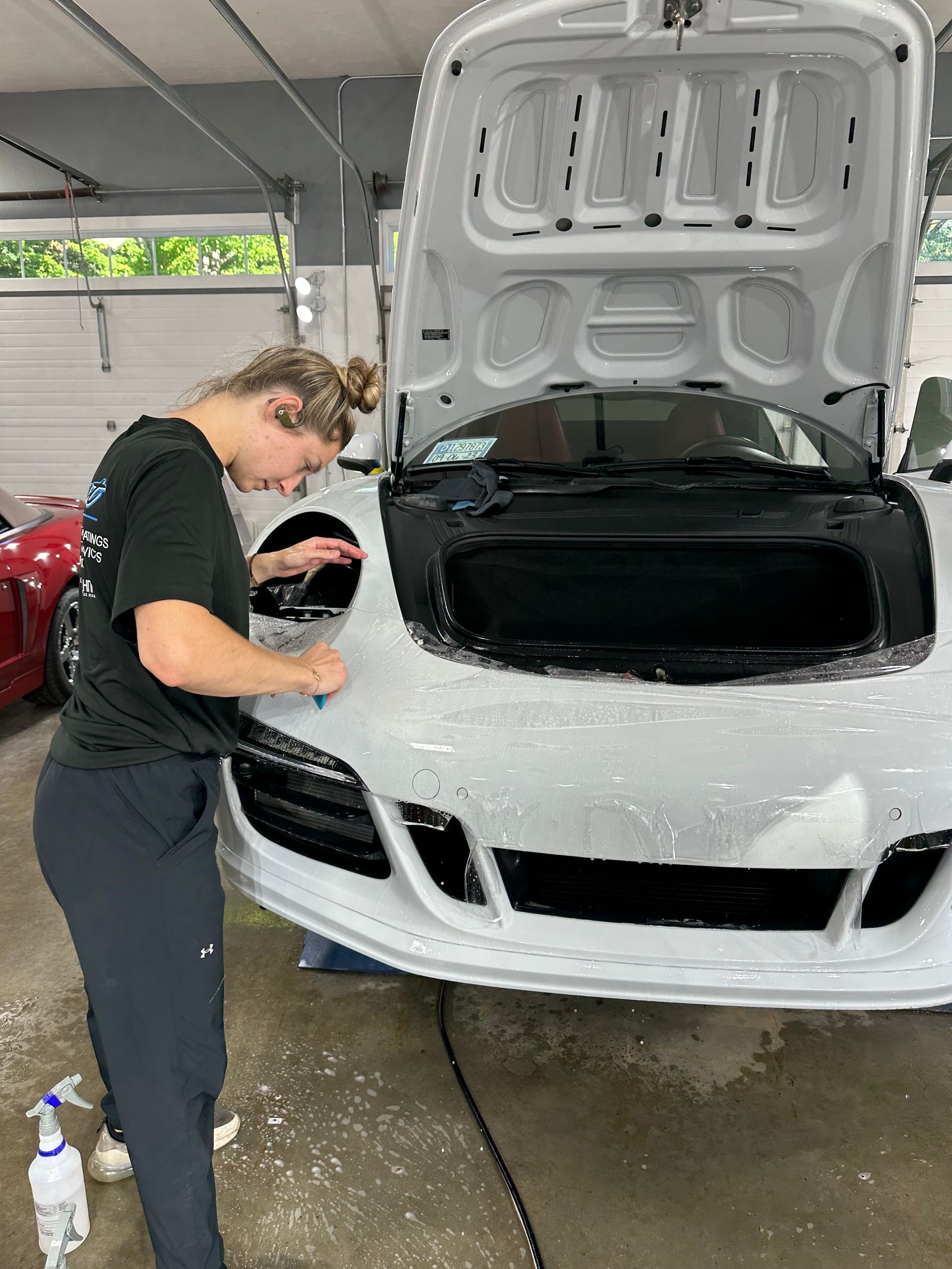 A woman is cleaning the front of a white sports car in a garage.