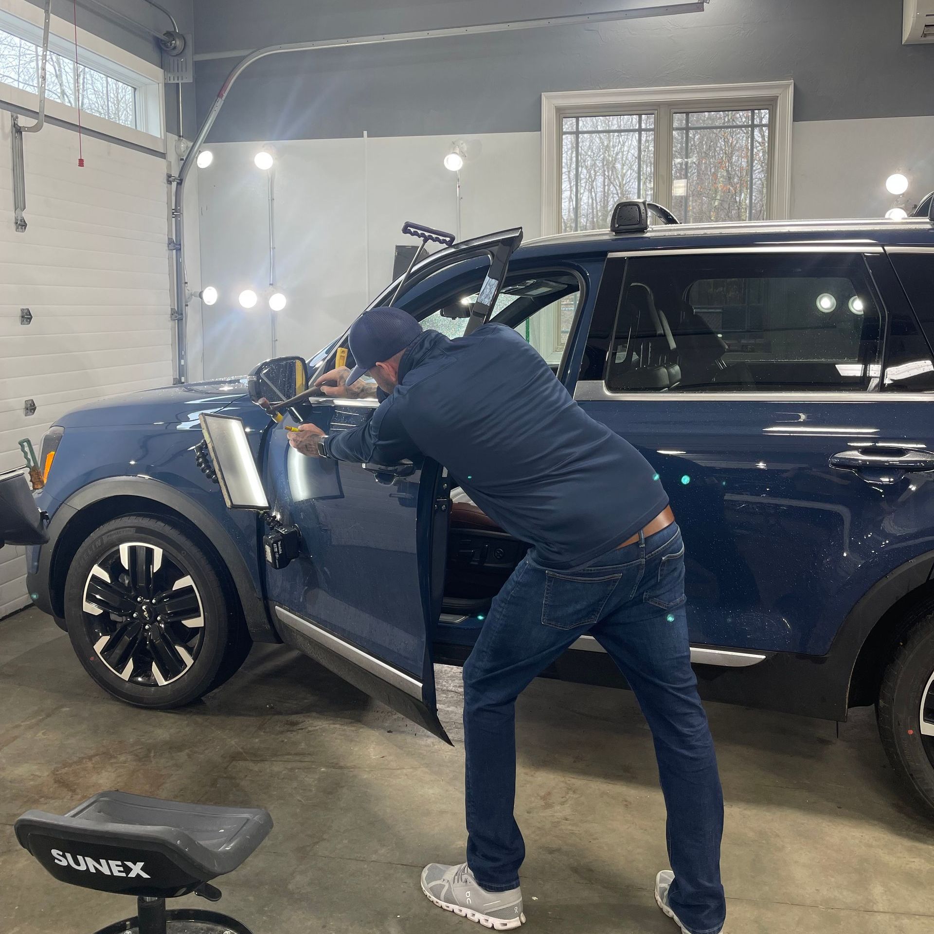 A man is standing next to a blue suv in a garage.