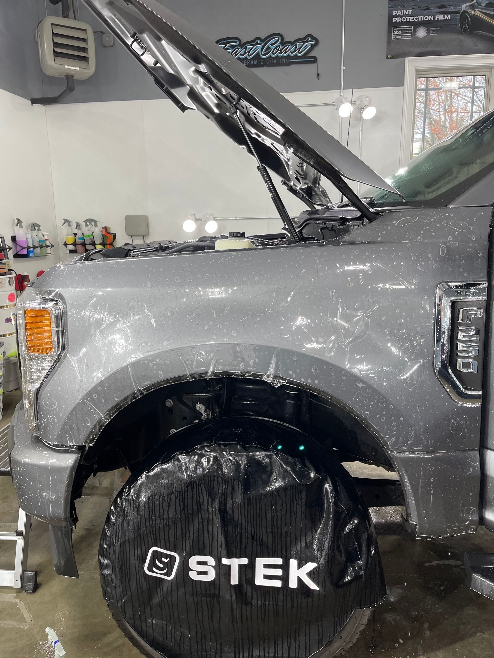 A gray truck with the hood up and a tire cover that says ostek