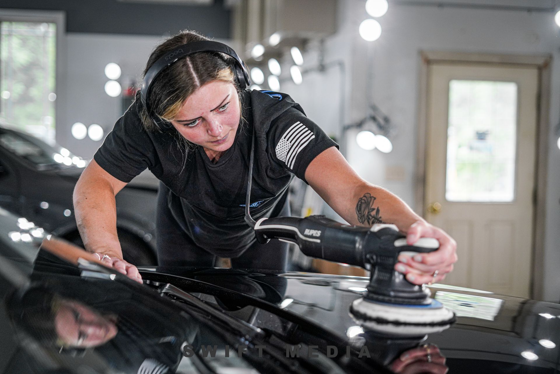 A woman is polishing the hood of a car in a garage.