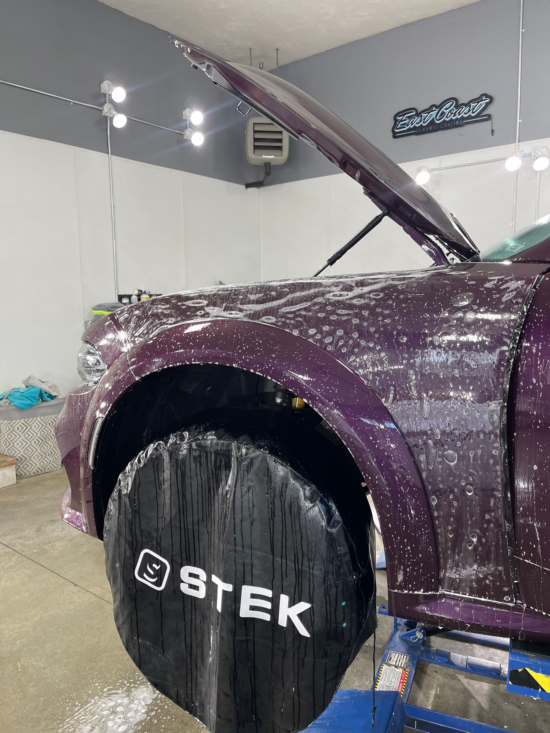 A purple car with the hood up is sitting in a garage.