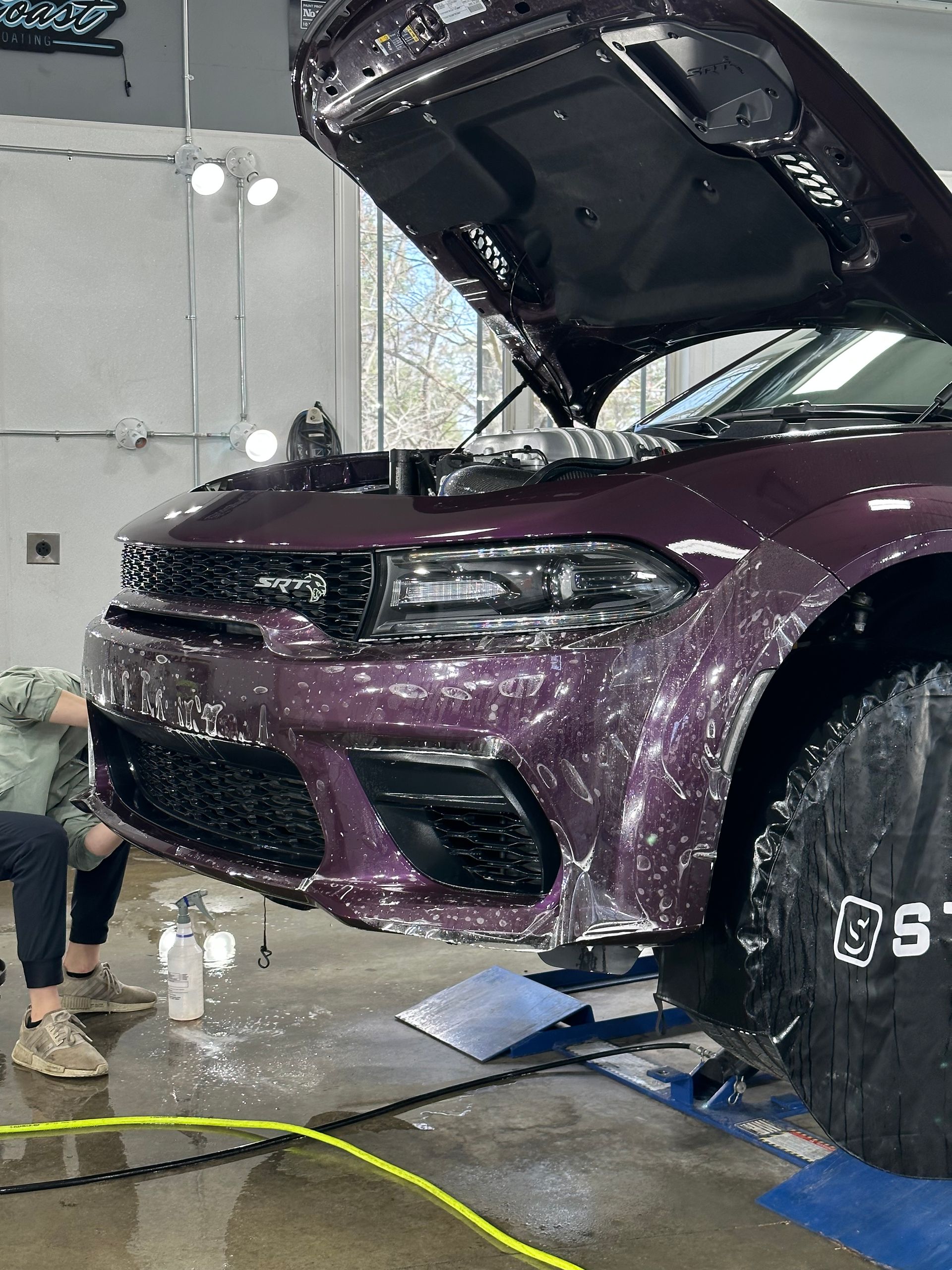 A man is cleaning a purple car with the hood open