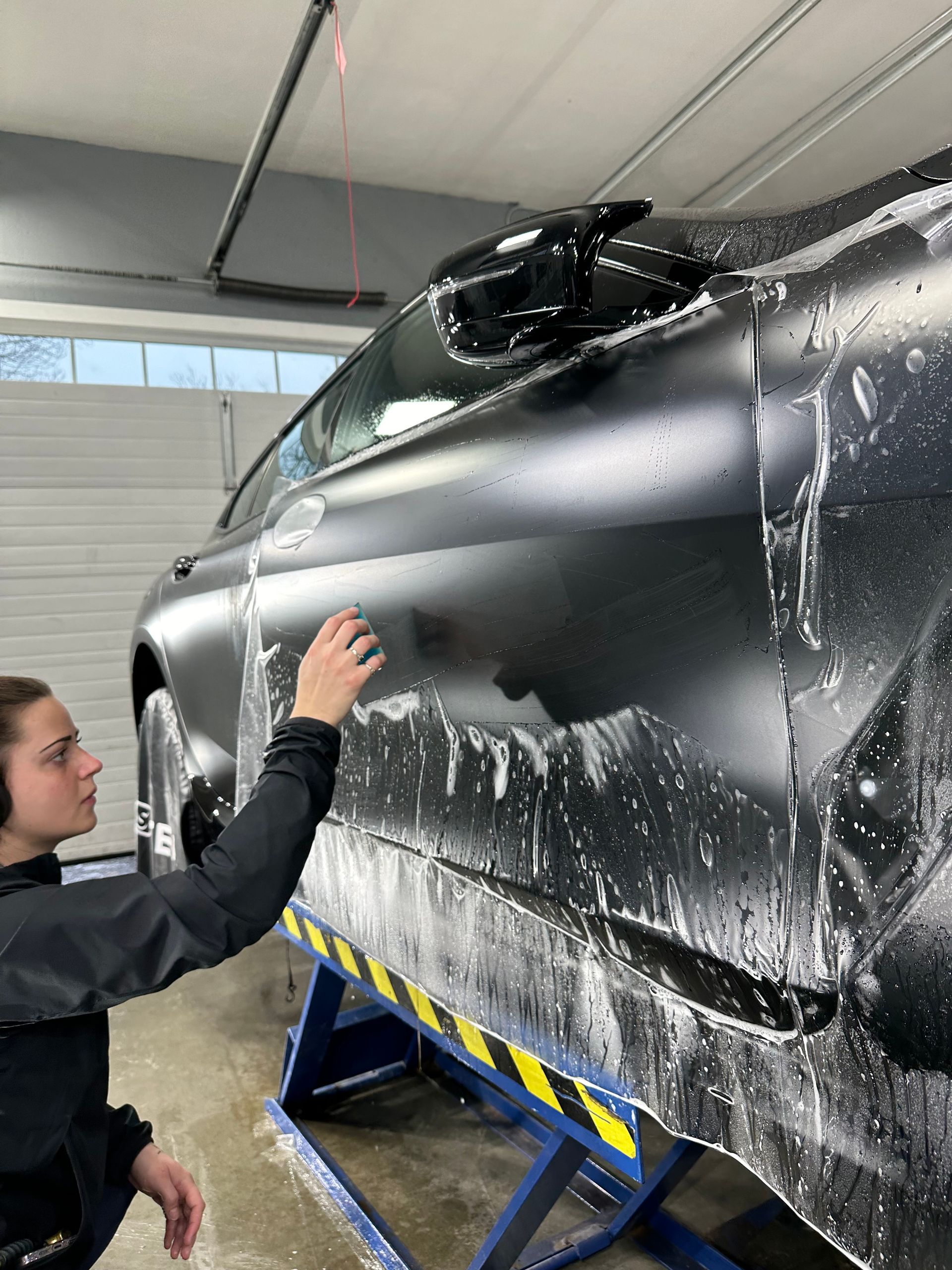 A man is washing a black car in a garage.