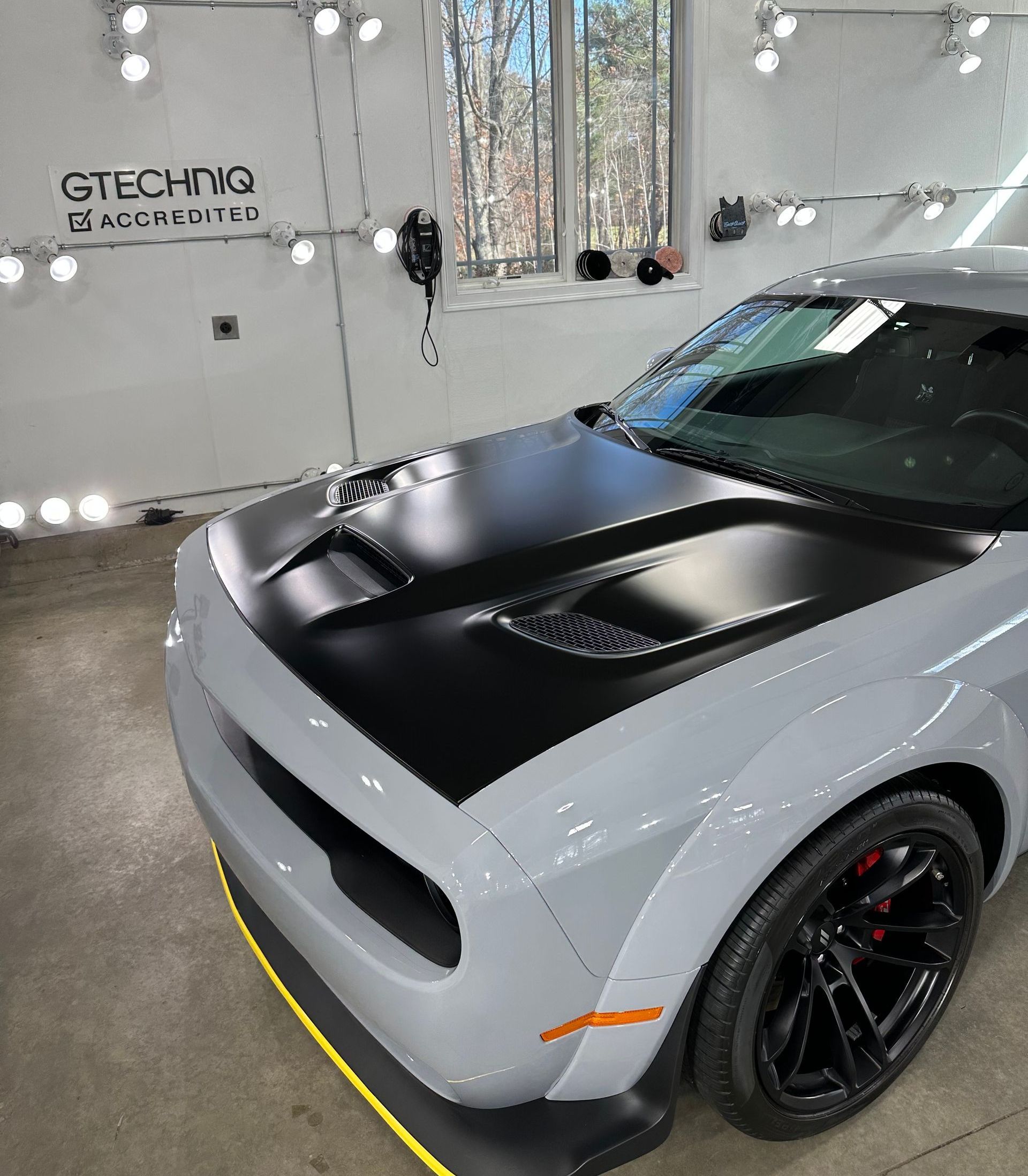 A white car with a black hood is parked in a garage.