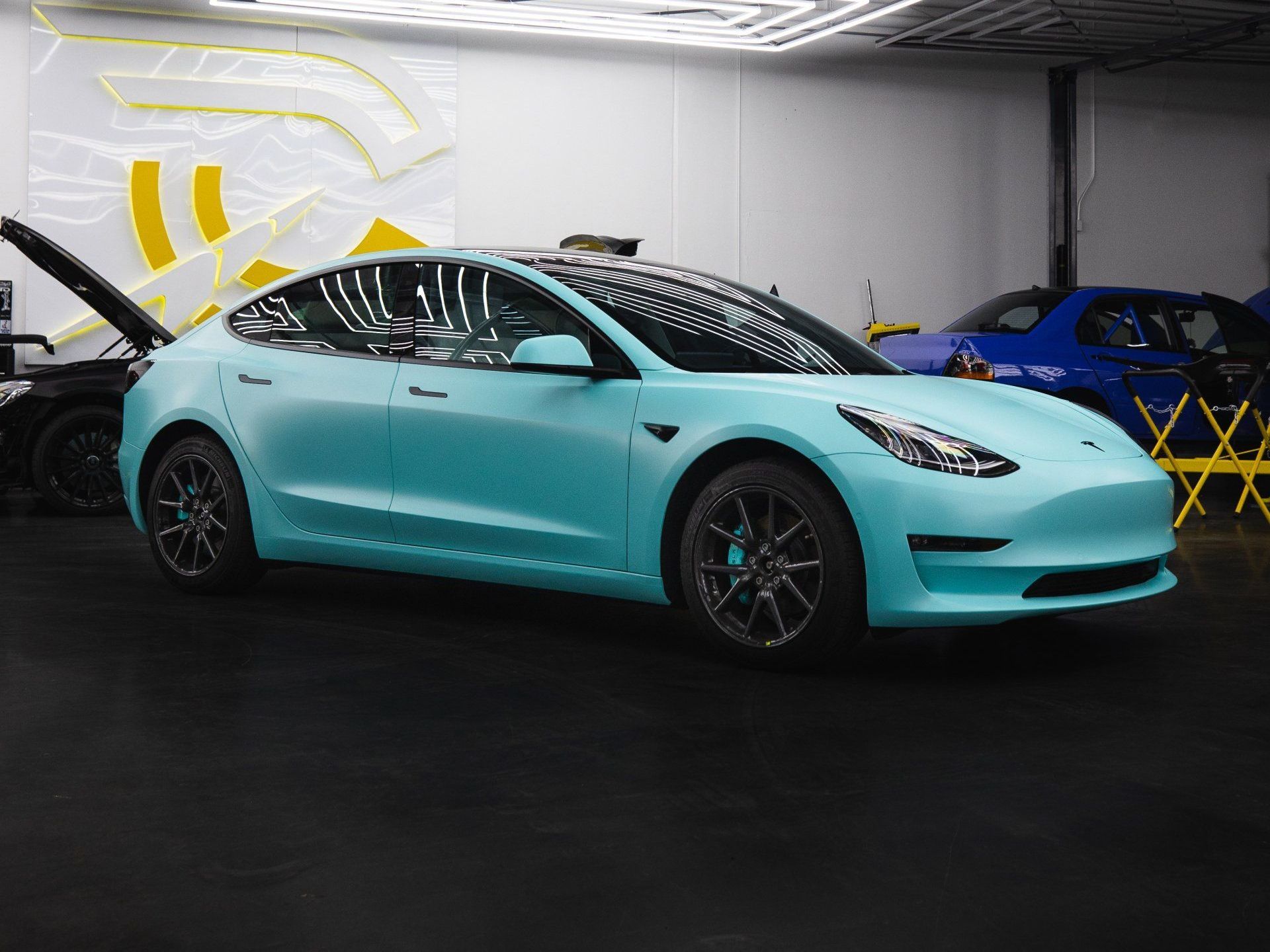 A blue tesla model 3 is parked in a garage.
