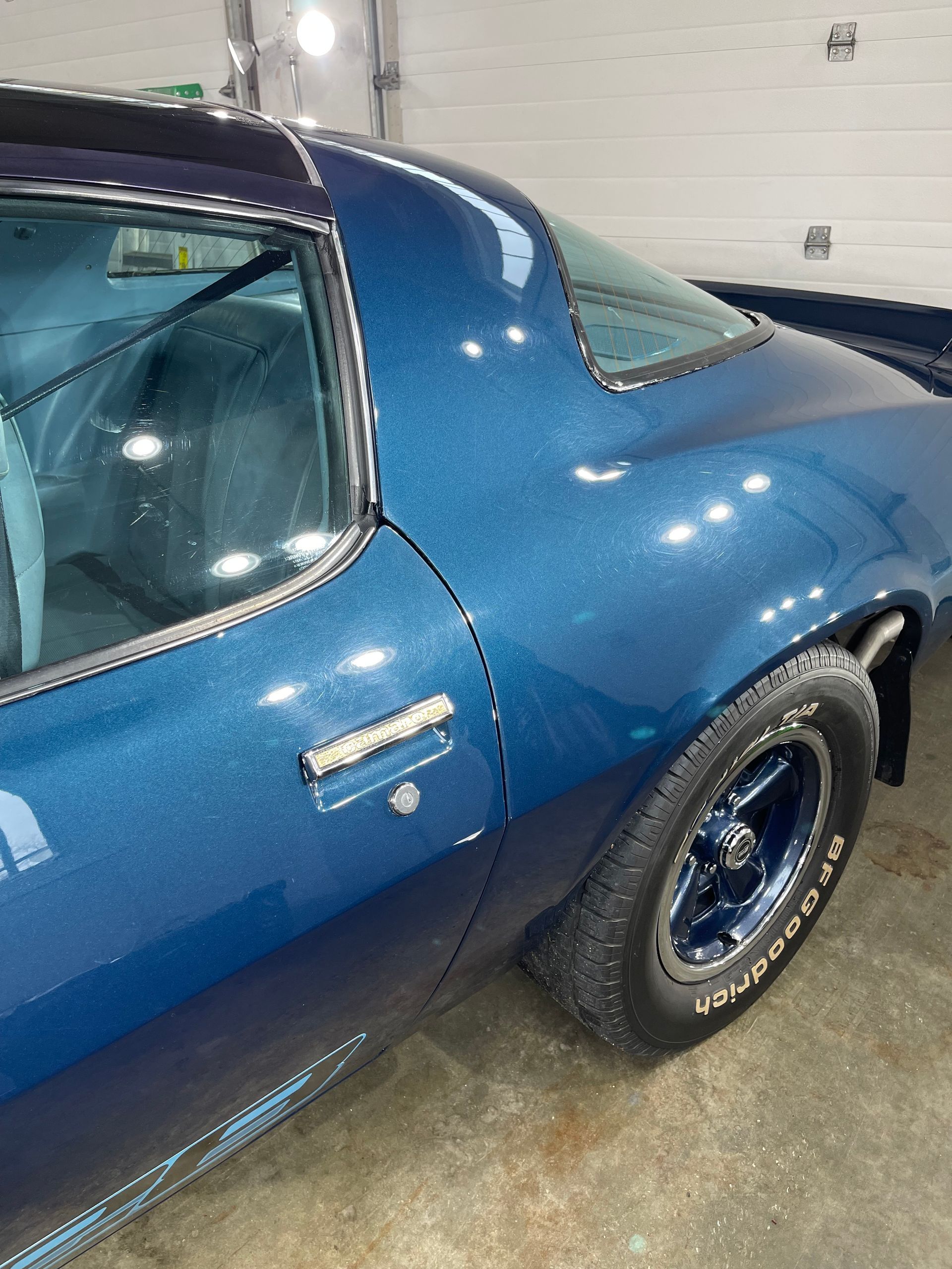 A blue car with a bfgoodrich tire is parked in a garage.