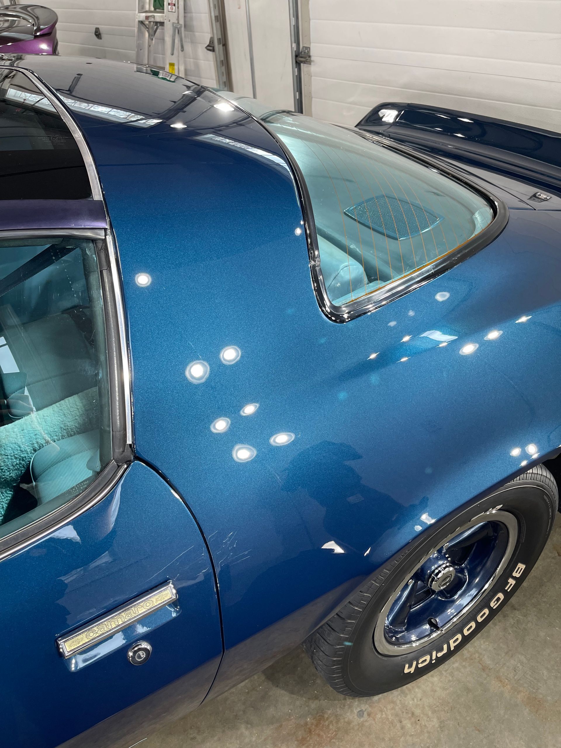 A blue car with a bfgoodrich tire is parked in a garage.